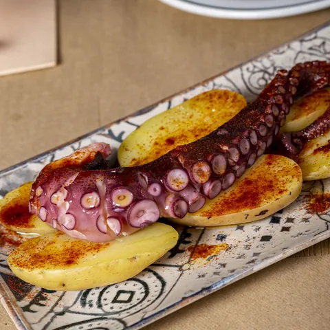 Pata de pulpo a la gallega sobre patatas con pimentón, en una fuente de cerámica.